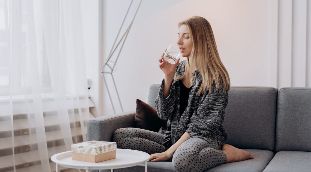 A woman sitting on a couch while drinking water